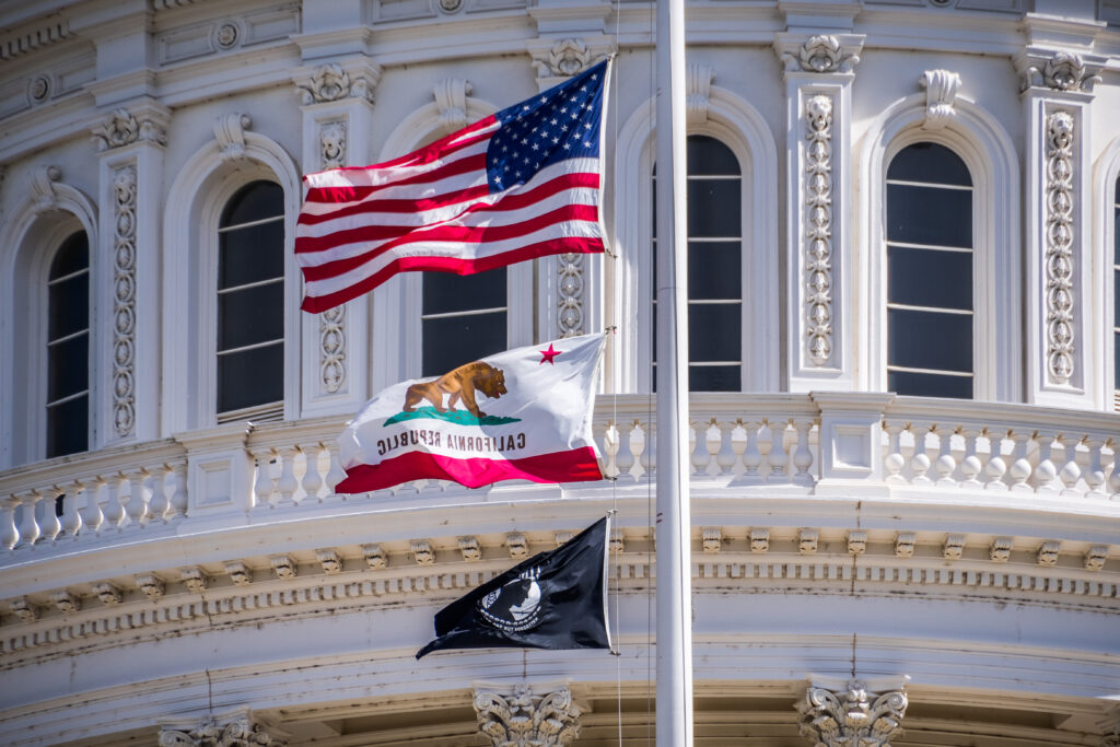 The U.S., California, and POW-MIA flags waving in the wind in front of the Capitol State Building in downtown Sacramento.
